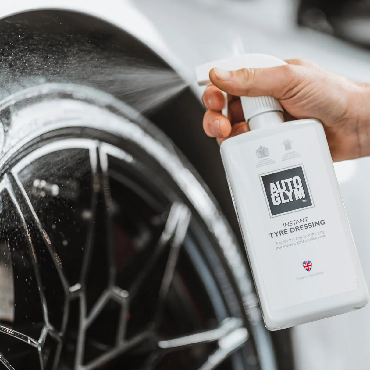 Autoglym Instant Tyre Dressing bottle next to a shiny black tyre, showcasing its sleek design and effective application.