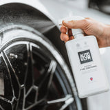 Autoglym Instant Tyre Dressing bottle next to a shiny black tyre, showcasing its sleek design and effective application.