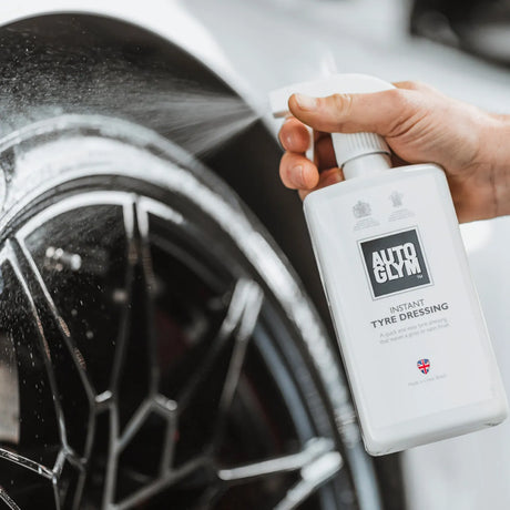 Autoglym Instant Tyre Dressing bottle next to a shiny black tyre, showcasing its sleek design and effective application.